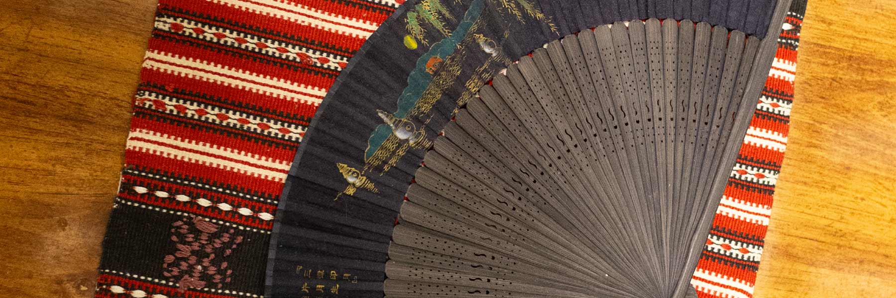 A delicately carved ornamental fan lies on top of a South American textile at the Ostrom Workshop, creating a pleasing textural contrast. 