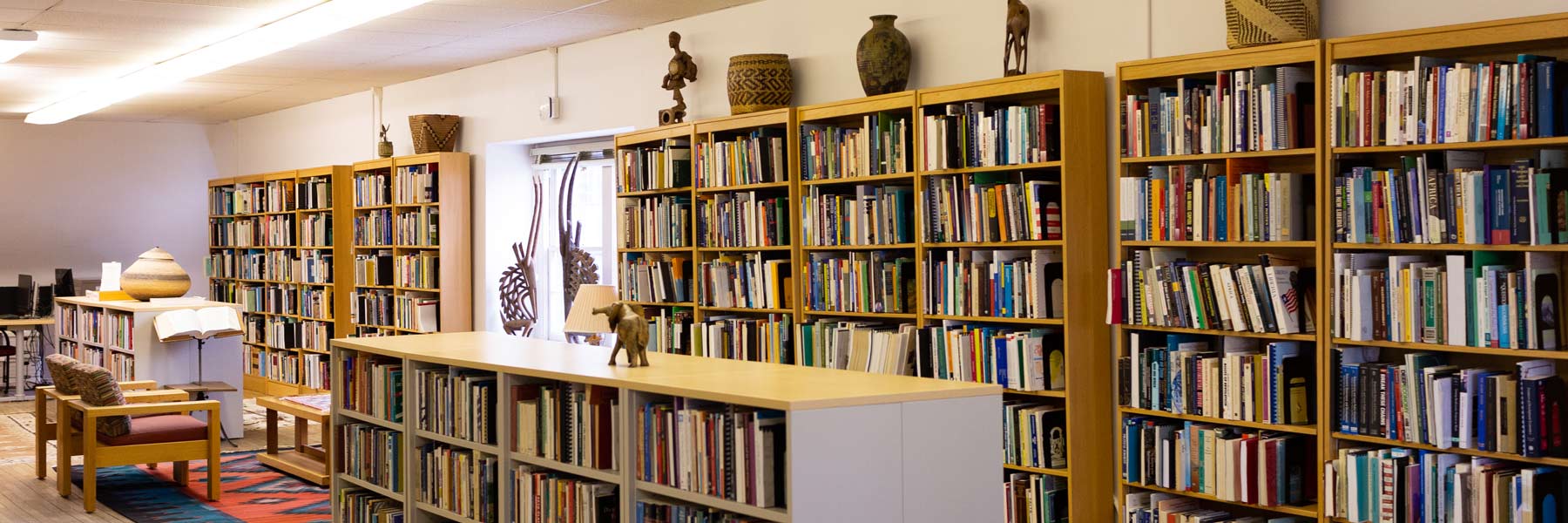 A long view of the Ostrom Workshop library, stuffed with comfortable furniture, textiles, and shelves upon shelves of books. 